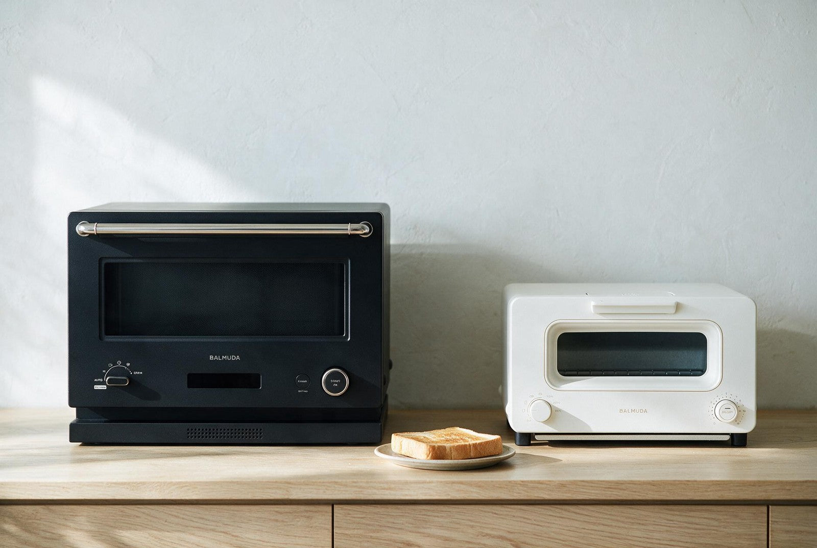 BALMUDA The Range microwave oven beside the smaller BALMUDA The Toaster on a pale oak kitchen counter, showing the size difference