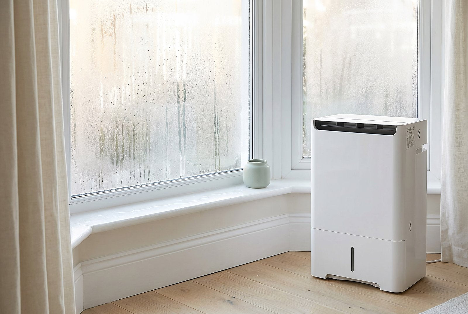 Condensation running down a UK bay window with a Mitsubishi dehumidifier beside it